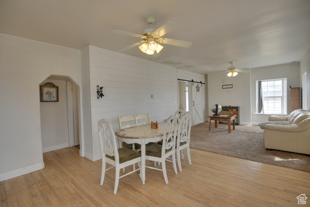 Dining room featuring baseboards, arched walkways, a barn door, a ceiling fan, and light wood-style floors