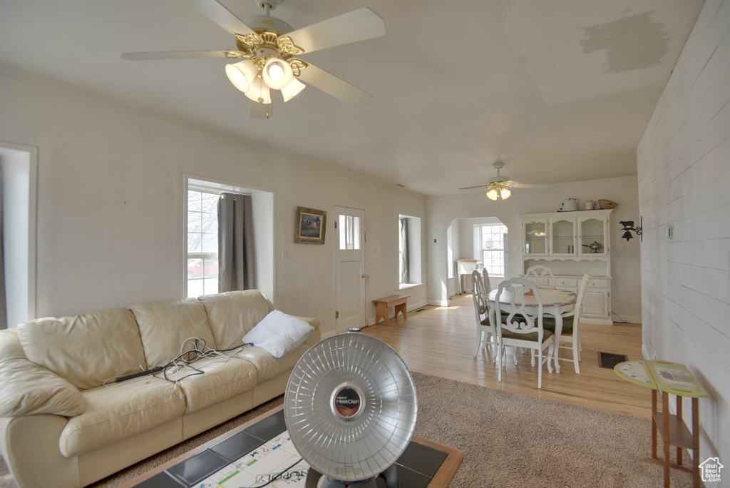 Living room with light wood finished floors, a ceiling fan, light carpet, and a healthy amount of sunlight