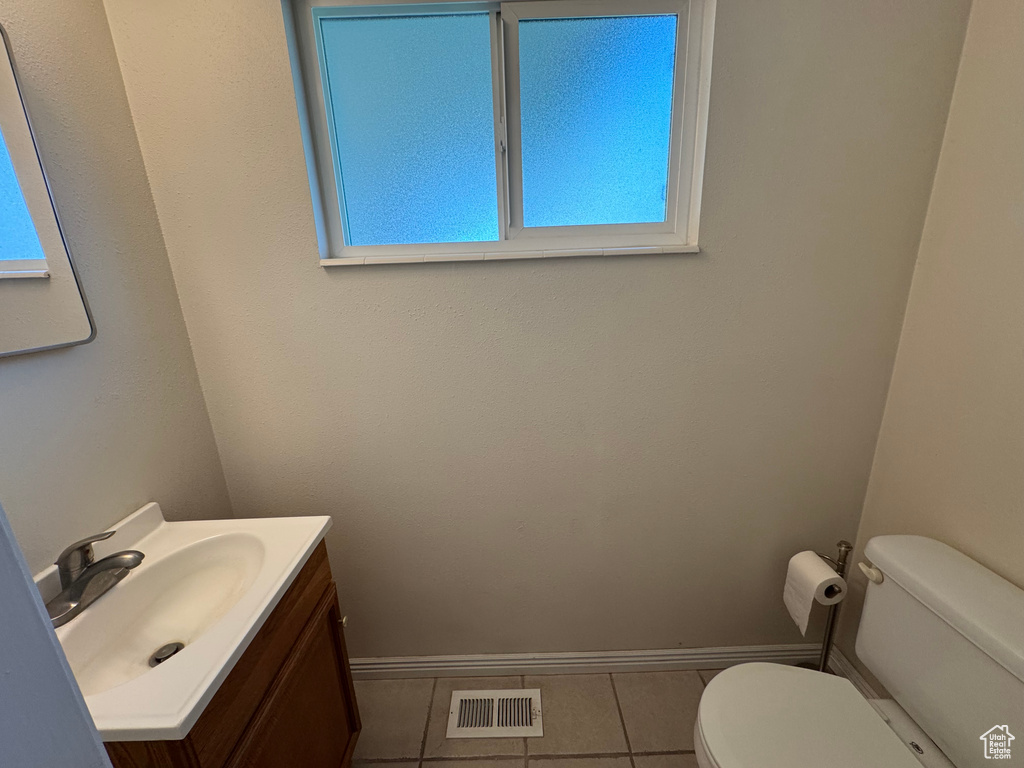 Half bathroom with vanity, tile patterned flooring, visible vents, toilet, and baseboards