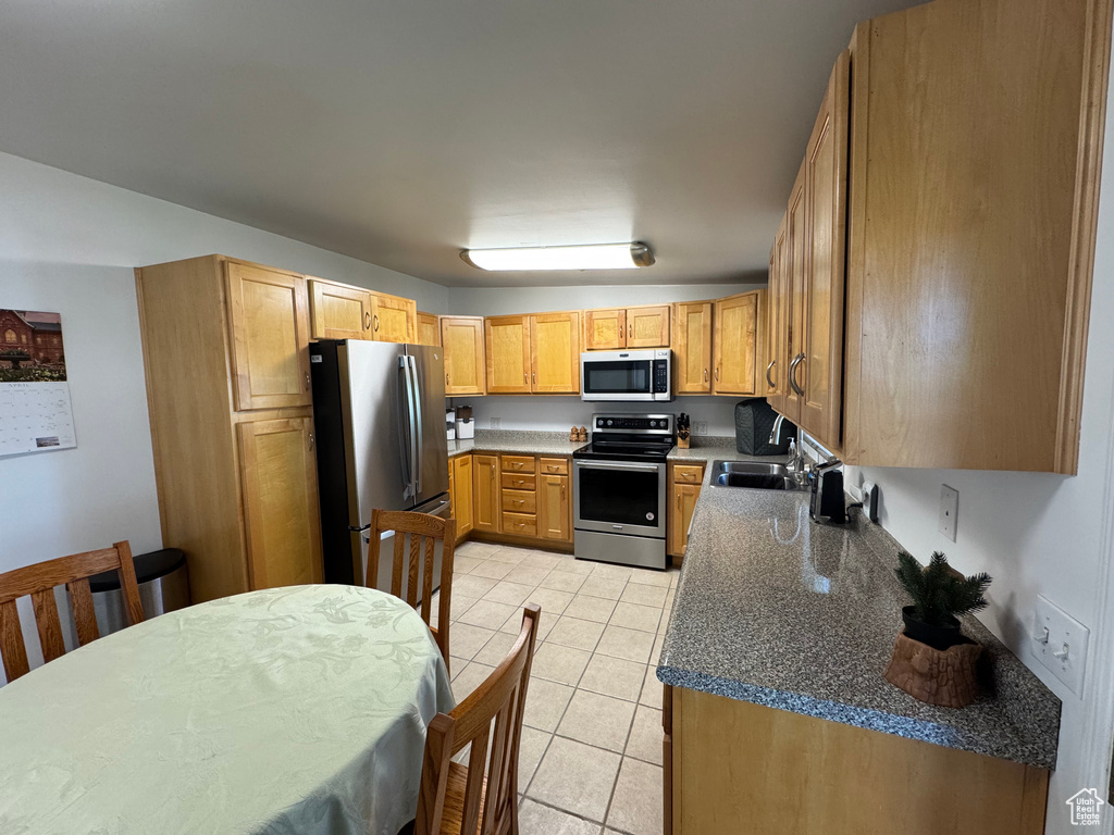 Kitchen with a sink, light tile patterned floors, dark countertops, and stainless steel appliances