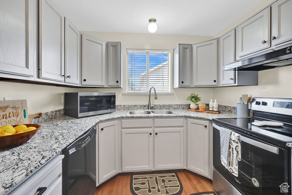 Kitchen featuring stainless steel appliances, under cabinet range hood, a sink, light wood-style flooring, and light stone countertops