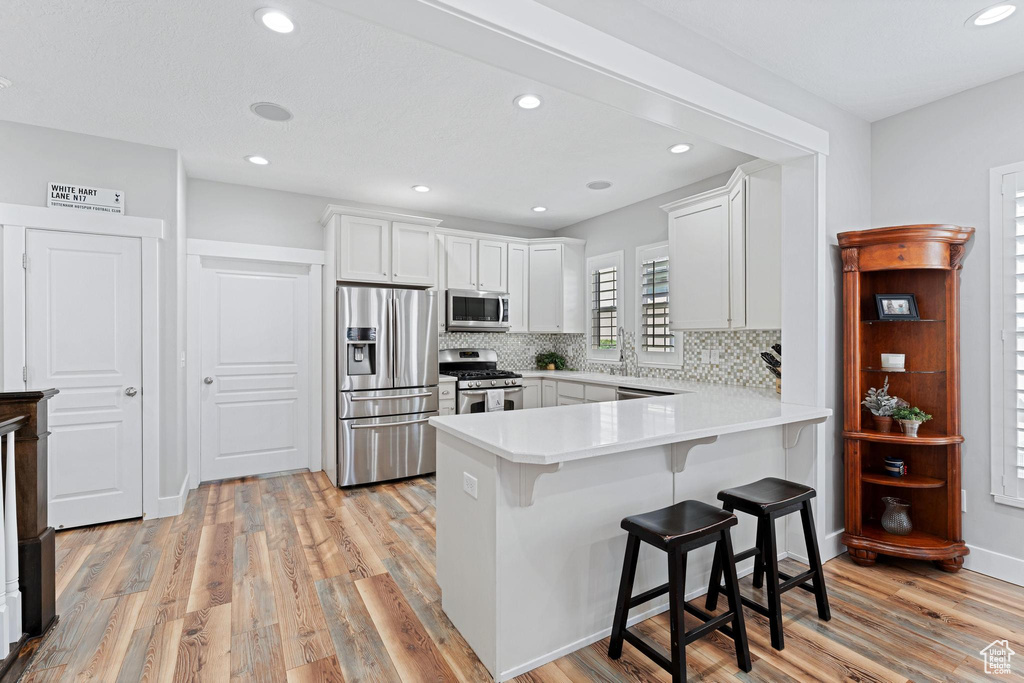 Kitchen featuring light countertops, light wood-type flooring, a breakfast bar, a peninsula, and stainless steel appliances