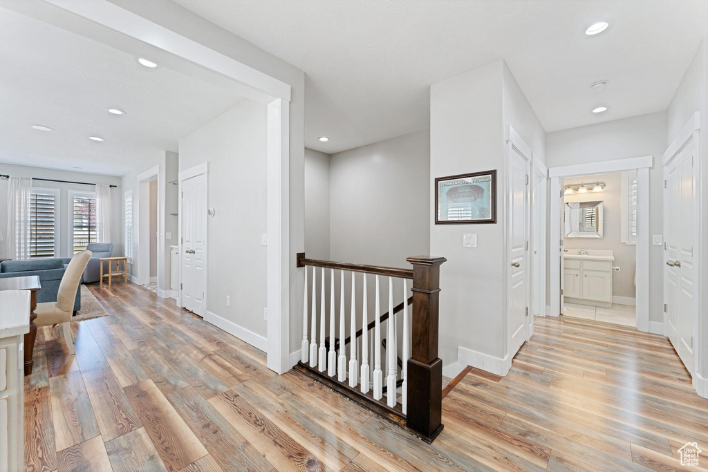 Hallway with an upstairs landing, baseboards, light wood-type flooring, and recessed lighting
