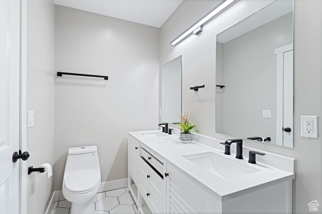 Bathroom with toilet, double vanity, a sink, and baseboards