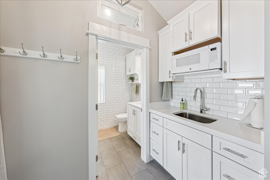Kitchen featuring light countertops, white microwave, light tile patterned floors, and a sink