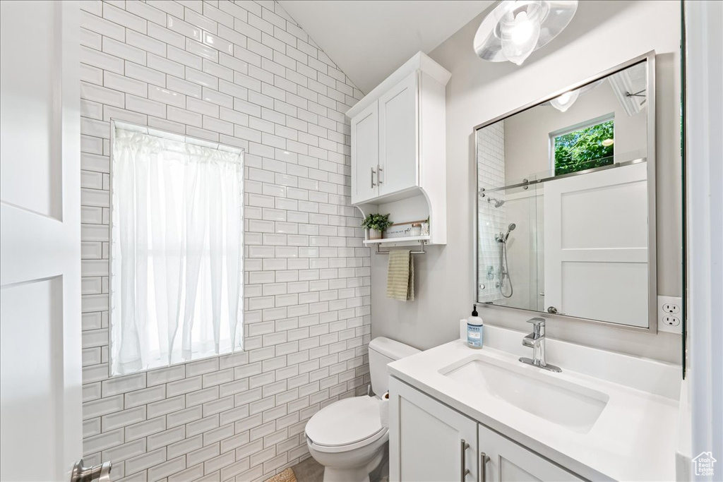 Full bath with vanity, toilet, a shower, lofted ceiling, and tile walls