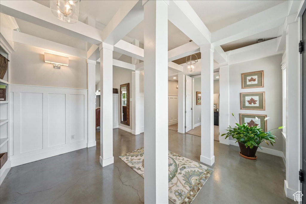 Entrance foyer with a decorative wall, a wainscoted wall, decorative columns, and finished concrete floors