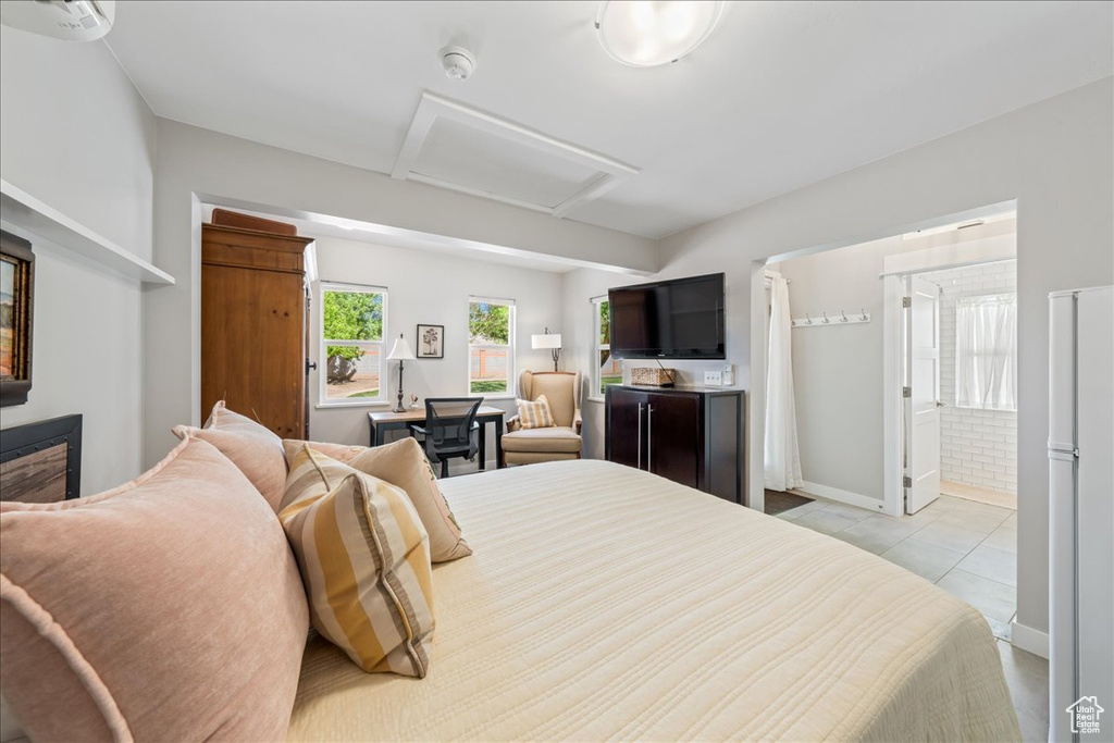 Bedroom featuring light tile patterned floors, baseboards, freestanding refrigerator, and attic access