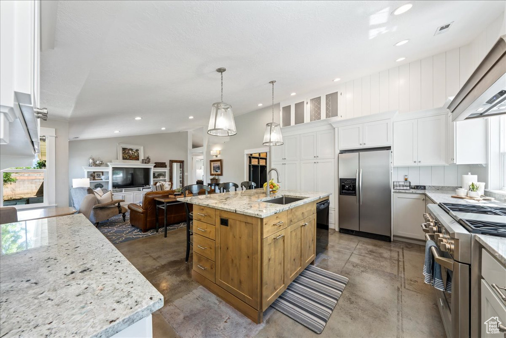 Kitchen featuring open floor plan, an island with sink, extractor fan, stainless steel appliances, and a sink