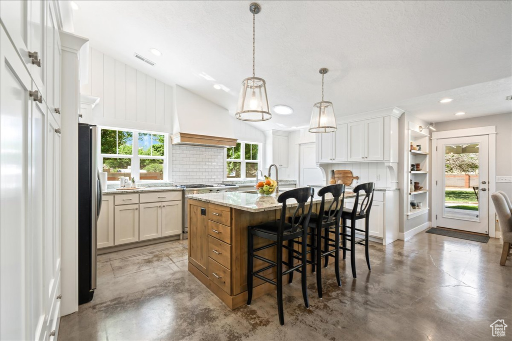 Kitchen with concrete floors, visible vents, a breakfast bar, premium range hood, and stainless steel appliances