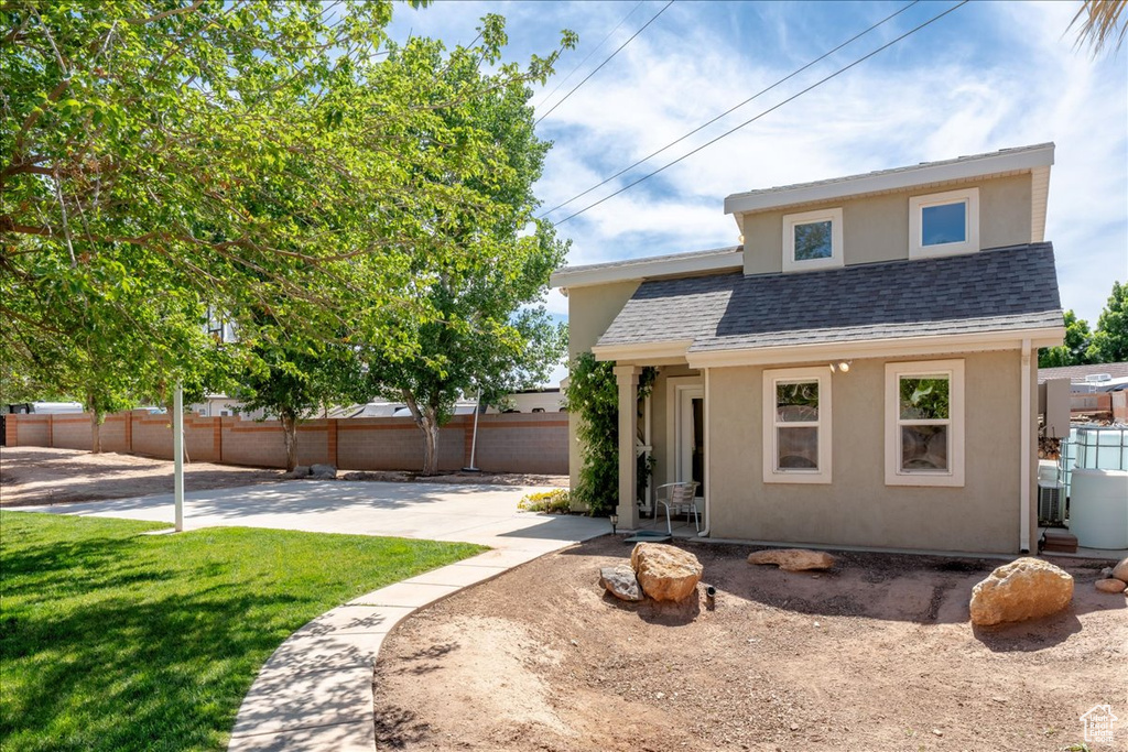 View of front of home featuring stucco siding, roof with shingles, a patio, fence, and a front lawn