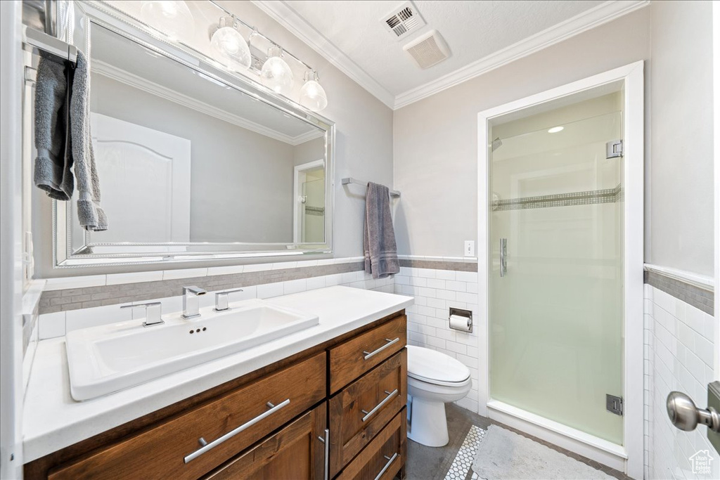 Full bath featuring ornamental molding, toilet, a shower stall, visible vents, and tile walls
