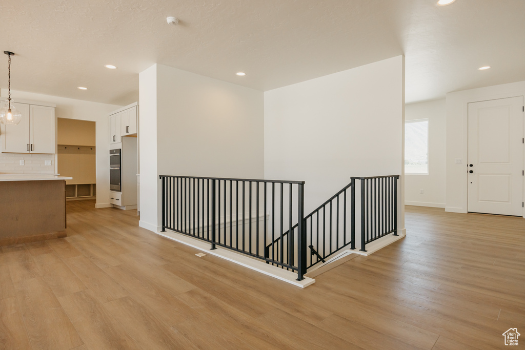 Corridor with an upstairs landing, light wood finished floors, recessed lighting, and baseboards