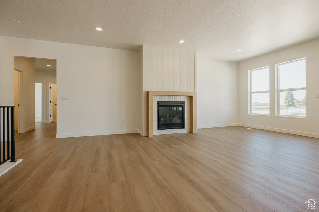 Unfurnished living room with light wood-style floors, recessed lighting, a tiled fireplace, baseboards, and a textured ceiling