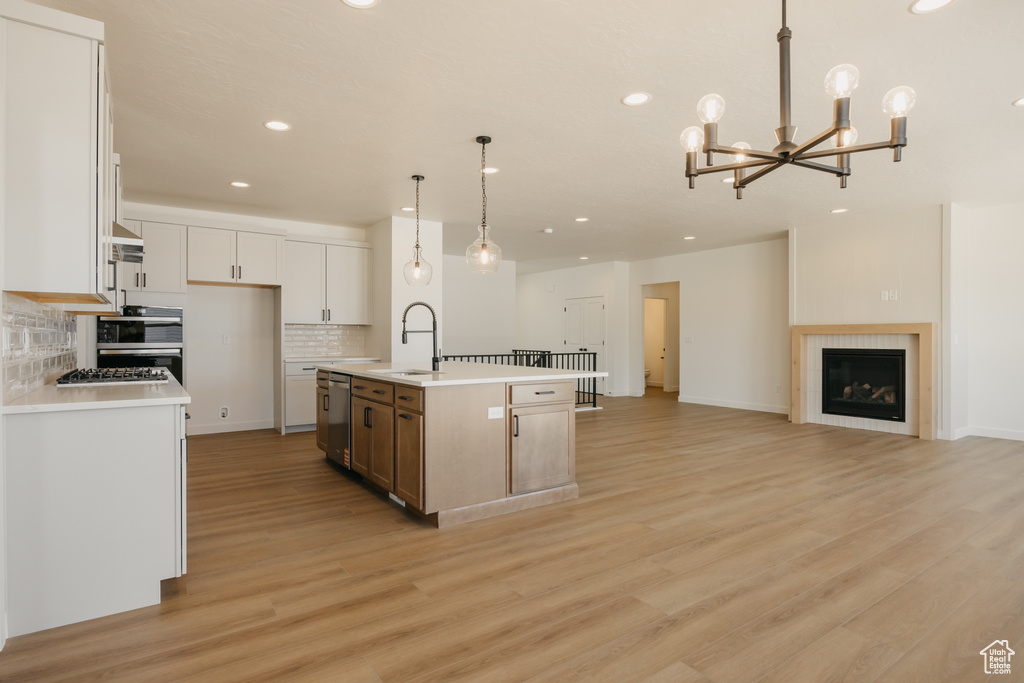 Kitchen with stainless steel dishwasher, a sink, recessed lighting, tasteful backsplash, and light wood-type flooring