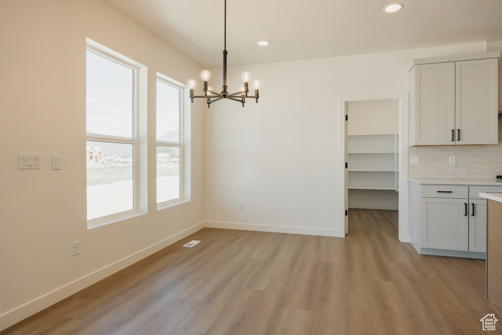 Unfurnished dining area with a chandelier, baseboards, light wood-type flooring, and recessed lighting
