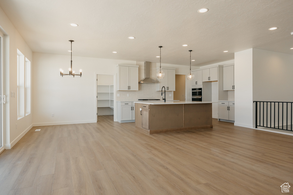 Kitchen featuring wall chimney range hood, a chandelier, recessed lighting, tasteful backsplash, and light wood finished floors