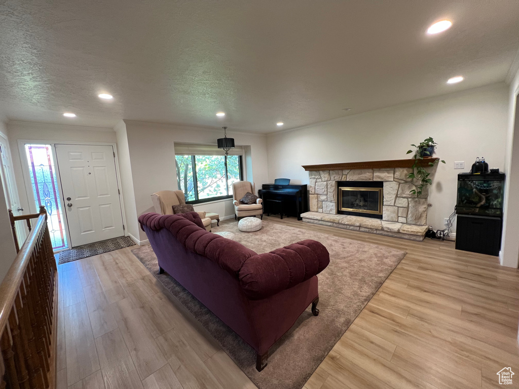 Living room featuring crown molding, a stone fireplace, recessed lighting, and wood finished floors