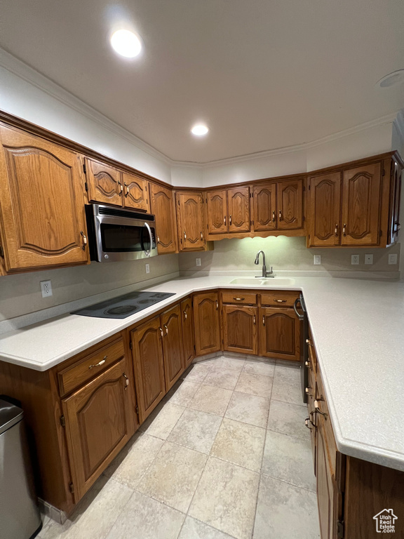 Kitchen featuring ornamental molding, stainless steel microwave, a sink, black electric stovetop, and brown cabinets