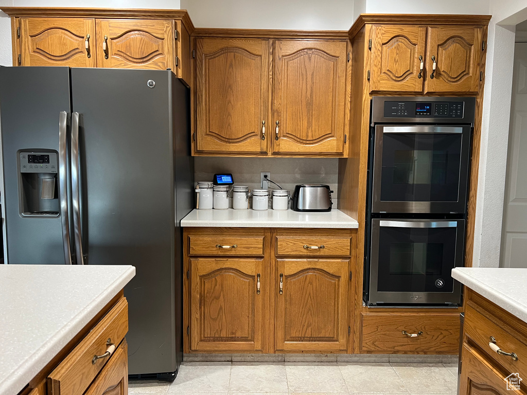 Kitchen featuring stainless steel fridge with ice dispenser, double wall oven, light countertops, and brown cabinetry