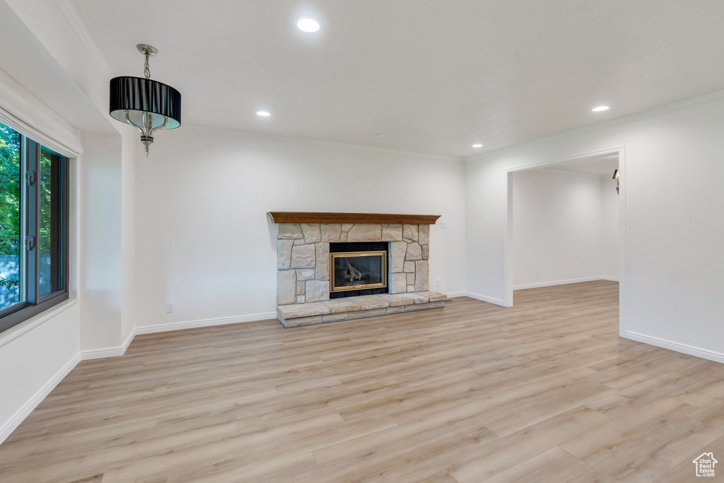 Unfurnished living room with light wood-type flooring, ornamental molding, recessed lighting, and a stone fireplace