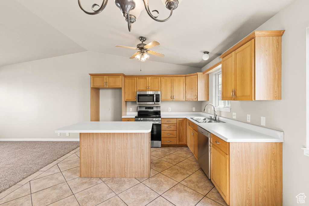 Kitchen with appliances with stainless steel finishes, light countertops, a kitchen island, lofted ceiling, and a sink