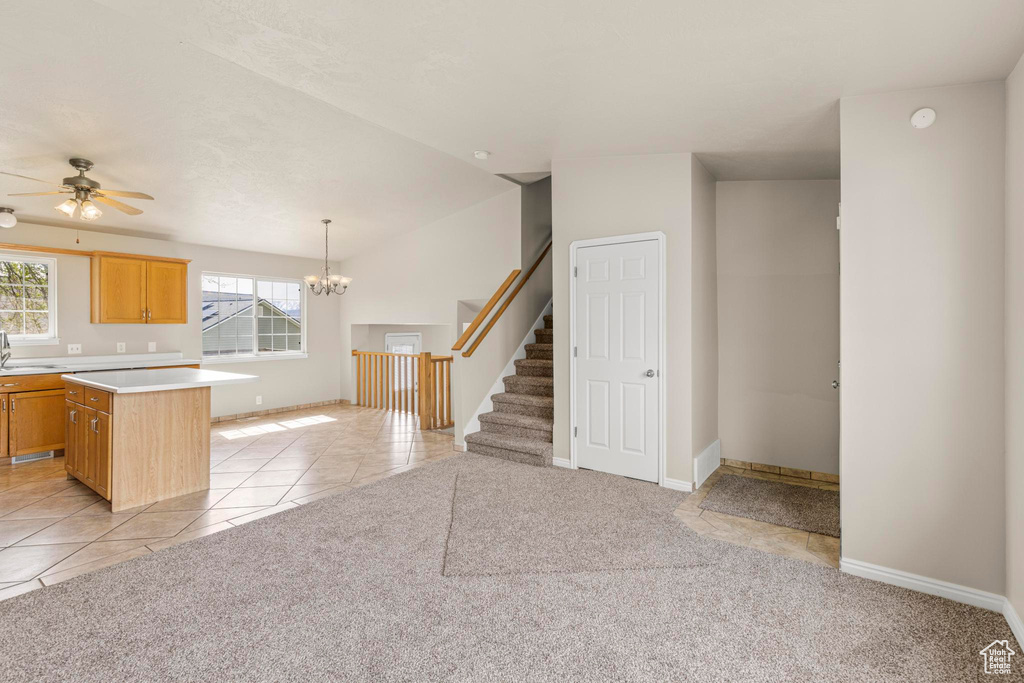 Unfurnished living room with ceiling fan with notable chandelier, light tile patterned floors, light colored carpet, stairs, and baseboards