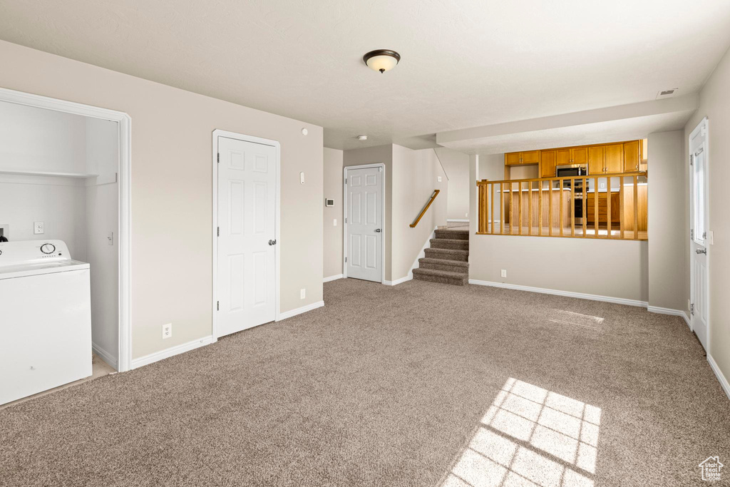 Unfurnished living room featuring baseboards, washer / dryer, carpet, and stairs