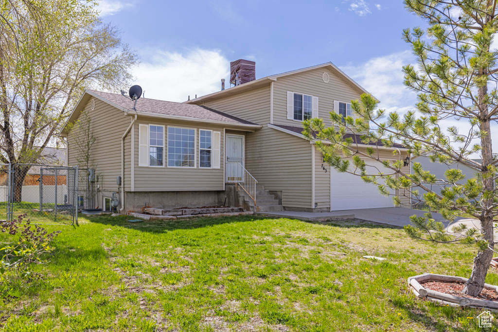 Back of property featuring a yard, fence, an attached garage, a chimney, and concrete driveway