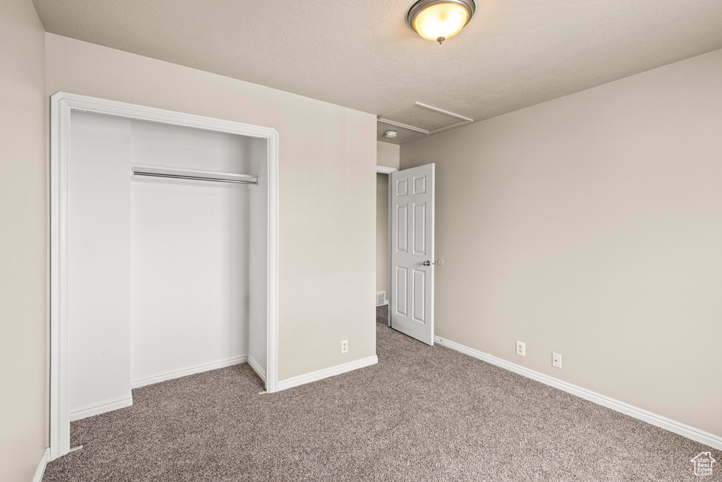 Unfurnished bedroom with carpet, attic access, a closet, and baseboards