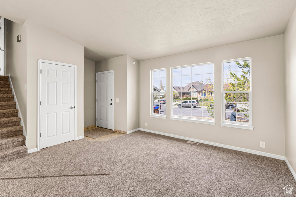 Carpeted spare room featuring visible vents, baseboards, and stairs