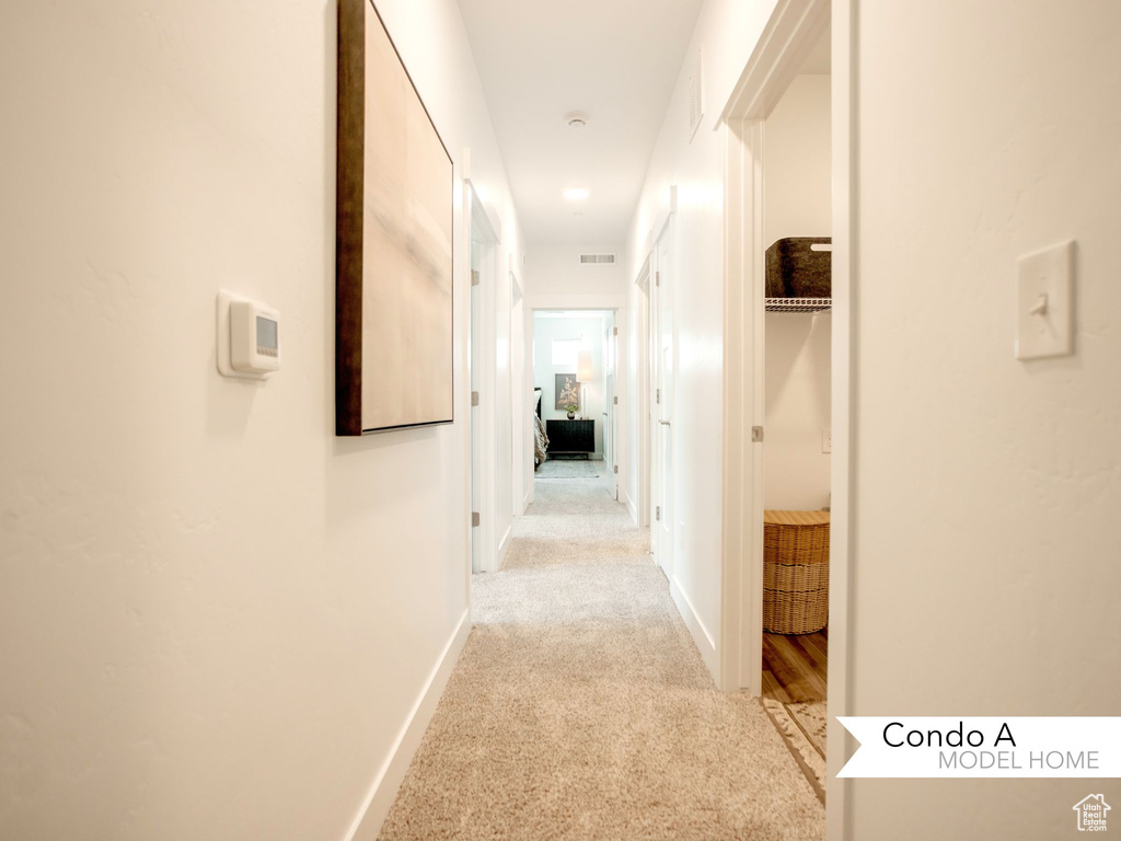 Corridor with visible vents, baseboards, and light colored carpet