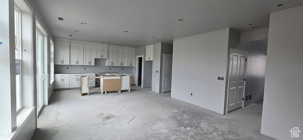 Kitchen with a kitchen island, white cabinetry, visible vents, and concrete flooring