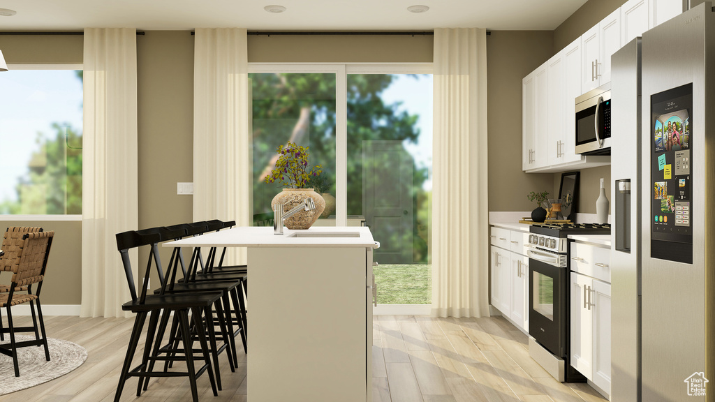 Kitchen with a kitchen bar, light wood-type flooring, white cabinets, appliances with stainless steel finishes, and light countertops