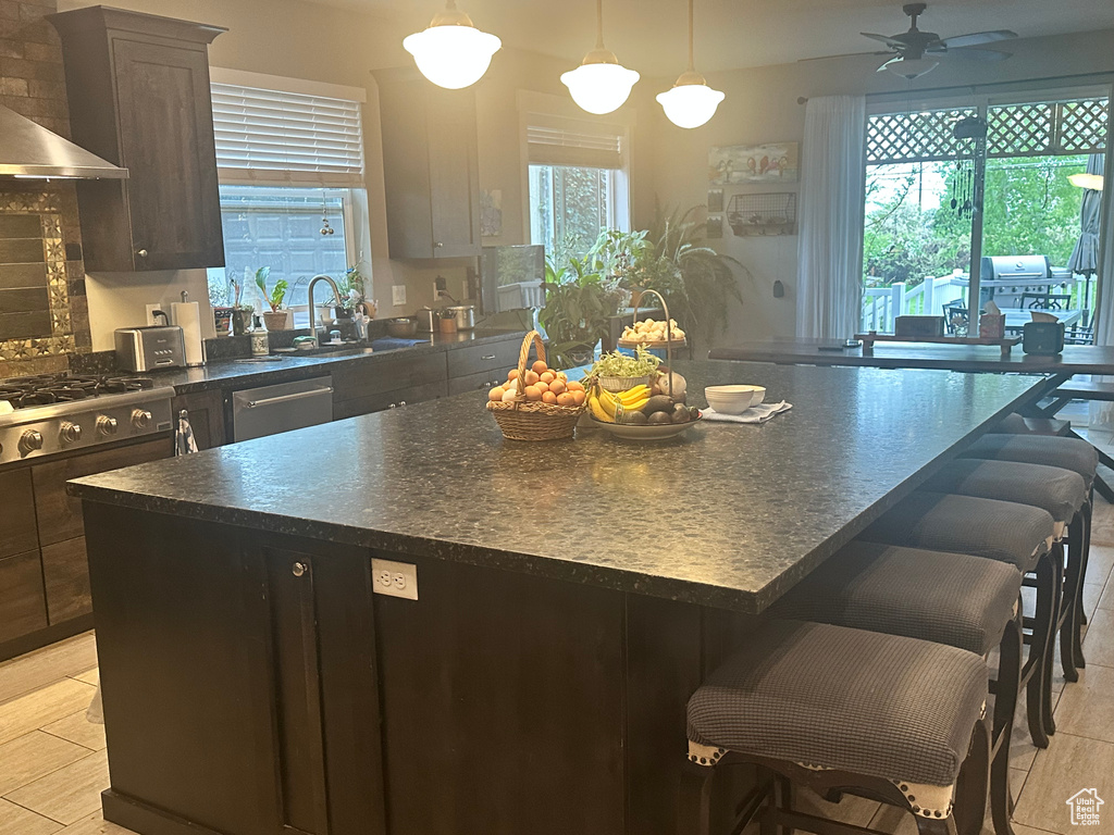 Kitchen featuring a center island, dark countertops, a breakfast bar, stainless steel appliances, and wall chimney exhaust hood
