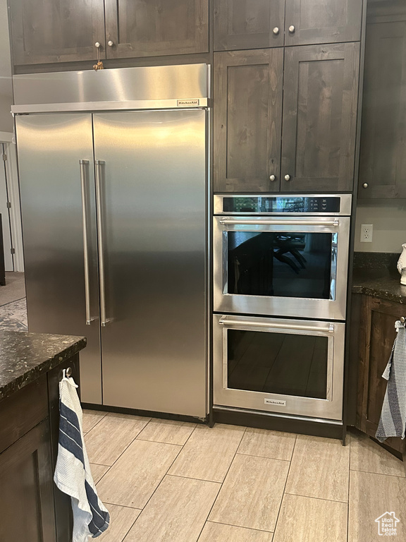 Kitchen featuring dark stone counters, wood finish floors, dark brown cabinetry, and stainless steel appliances