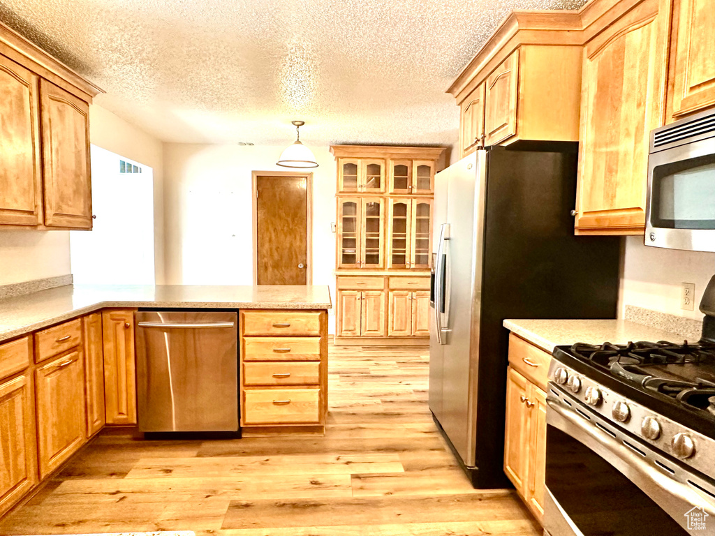 Kitchen featuring stainless steel appliances, light wood-style floors, a peninsula, a textured ceiling, and decorative light fixtures