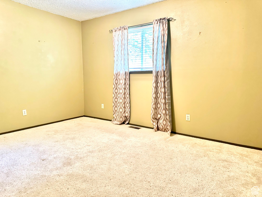 Carpeted spare room featuring a textured ceiling and baseboards