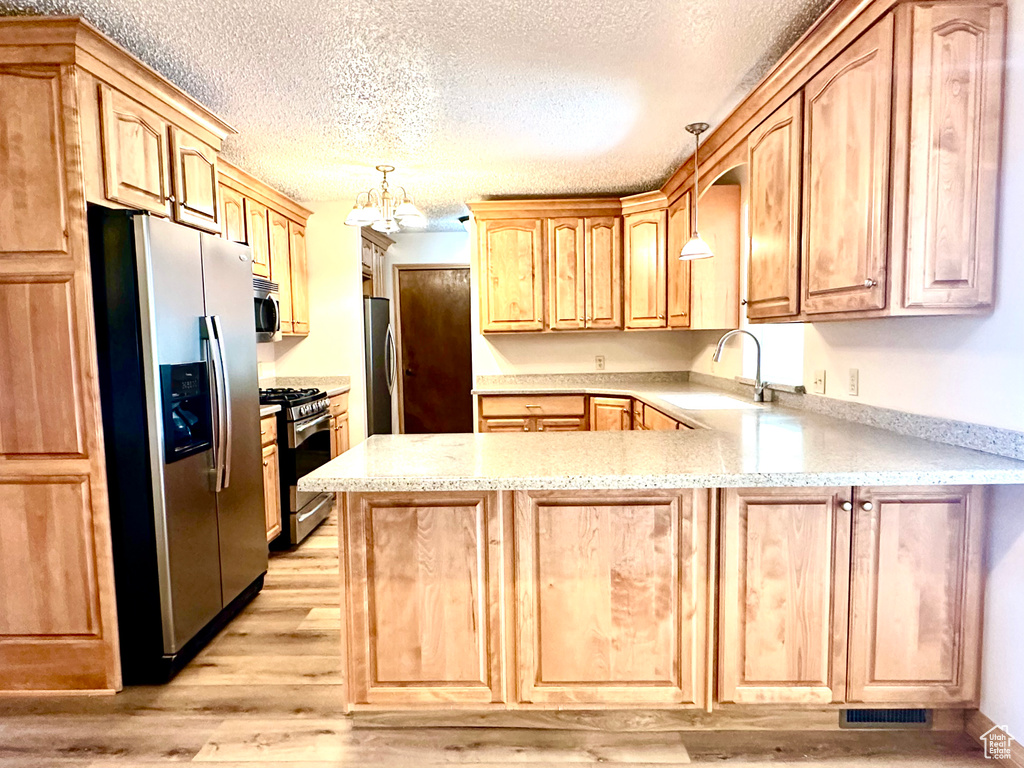 Kitchen featuring stainless steel appliances, a sink, a peninsula, light wood-style flooring, and a textured ceiling