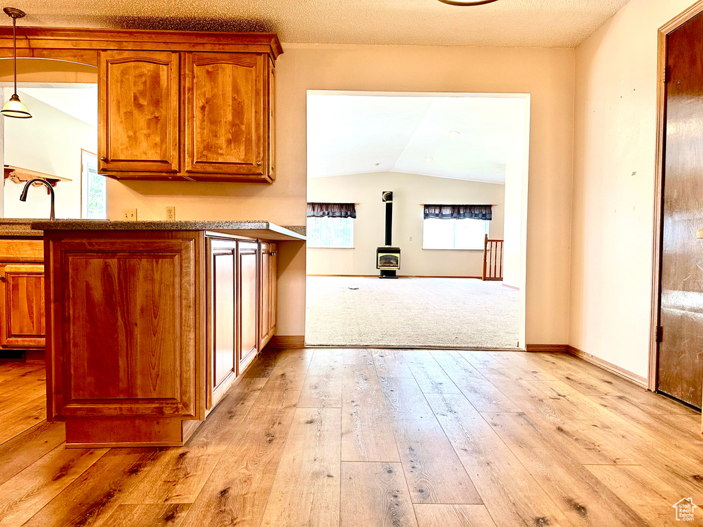 Kitchen featuring a wood stove, brown cabinetry, light wood finished floors, lofted ceiling, and decorative light fixtures