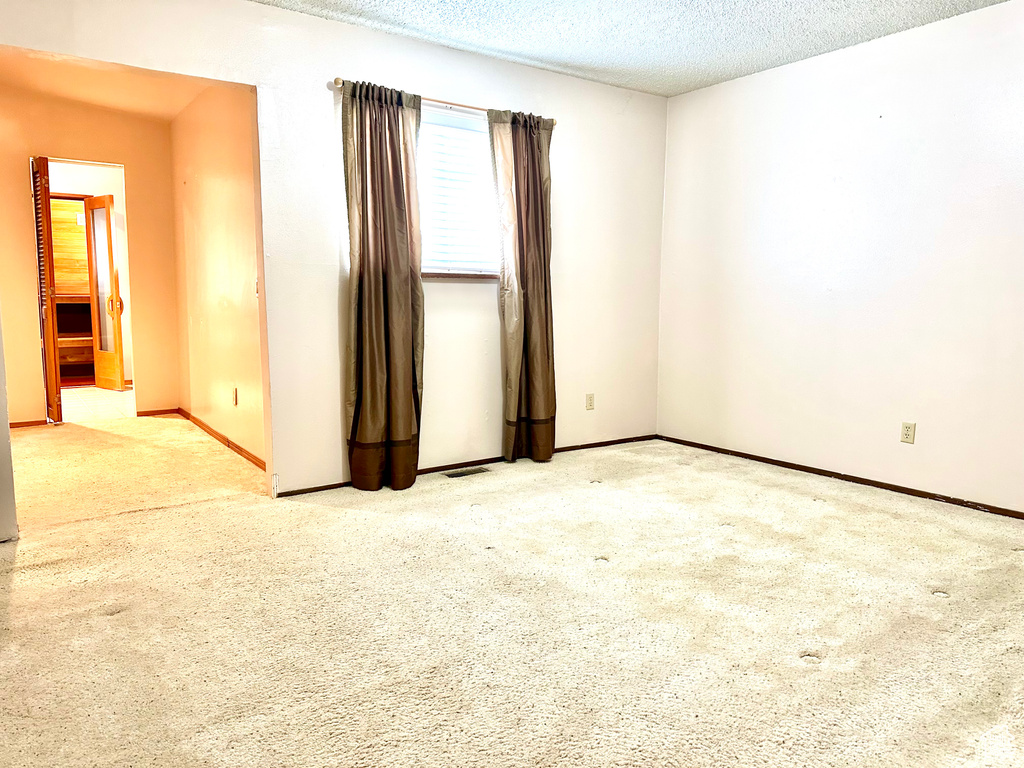 Carpeted spare room with a textured ceiling and baseboards
