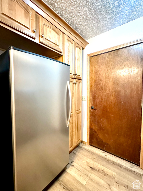Kitchen with freestanding refrigerator, light wood-type flooring, a textured ceiling, and light brown cabinets