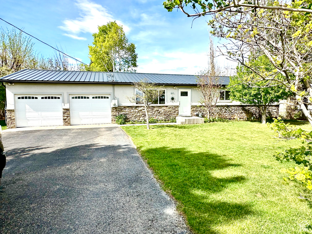 Single story home featuring stucco siding, stone siding, asphalt driveway, and a front yard