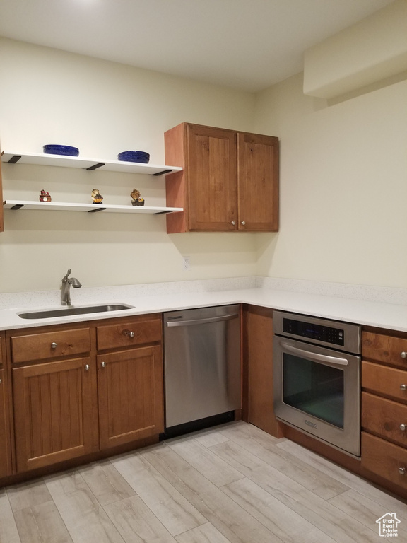 Kitchen featuring appliances with stainless steel finishes, a sink, open shelves, light wood finished floors, and brown cabinetry