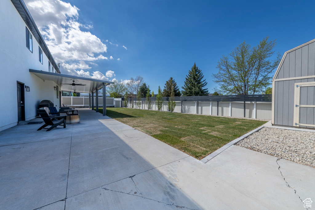 View of yard with a storage unit, a fenced backyard, an outbuilding, a patio area, and a ceiling fan