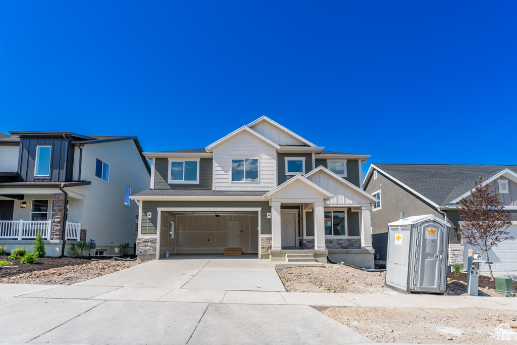 View of front of house with concrete driveway, stone siding, a porch, and an attached garage