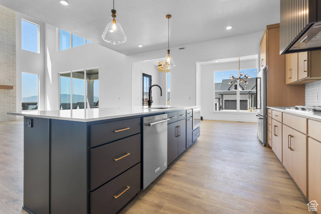 Kitchen with appliances with stainless steel finishes, a sink, wall chimney range hood, a center island with sink, and light countertops