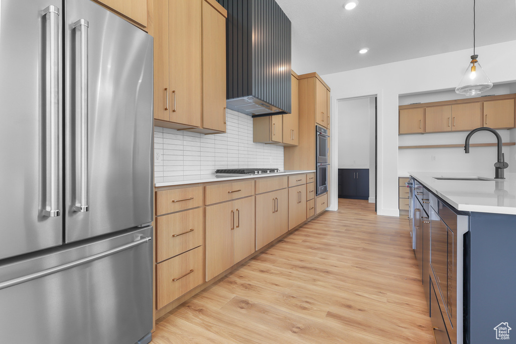 Kitchen with stainless steel appliances, a sink, light wood finished floors, light countertops, and wall chimney range hood