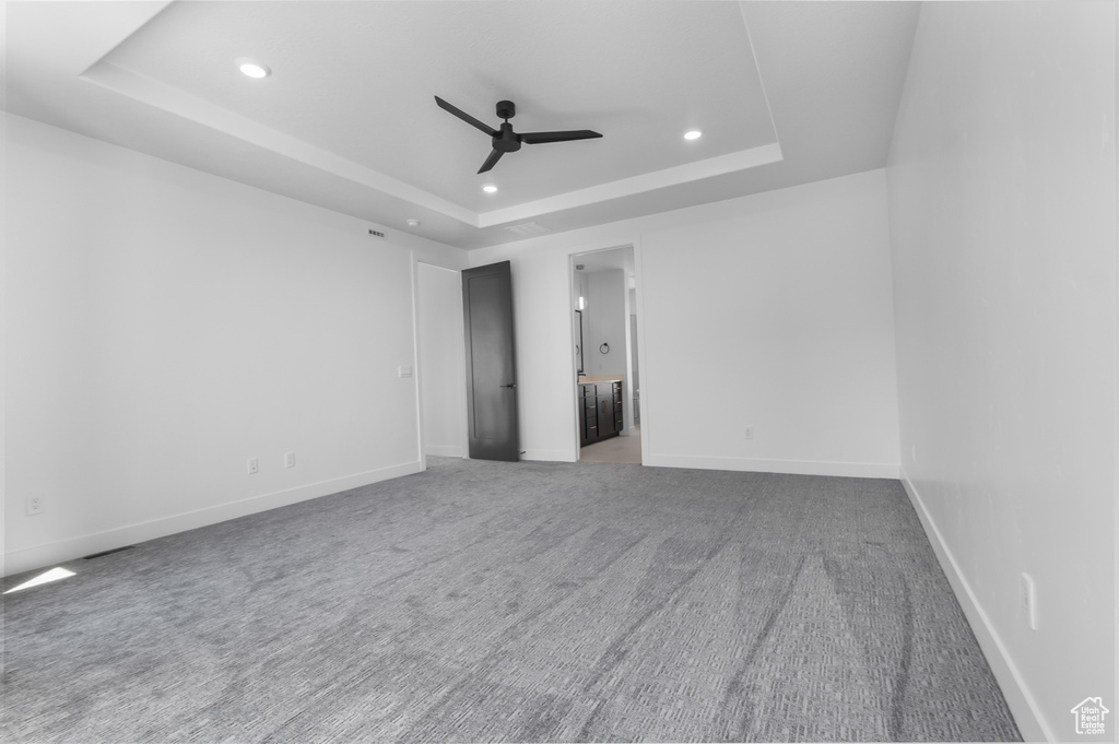 Carpeted empty room featuring a raised ceiling, ceiling fan, recessed lighting, and baseboards