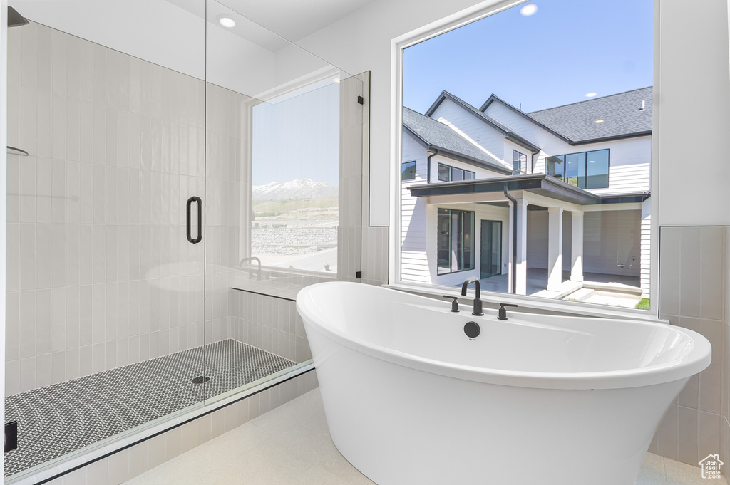 Full bath with tile walls, plenty of natural light, a freestanding bath, a stall shower, and tile patterned flooring